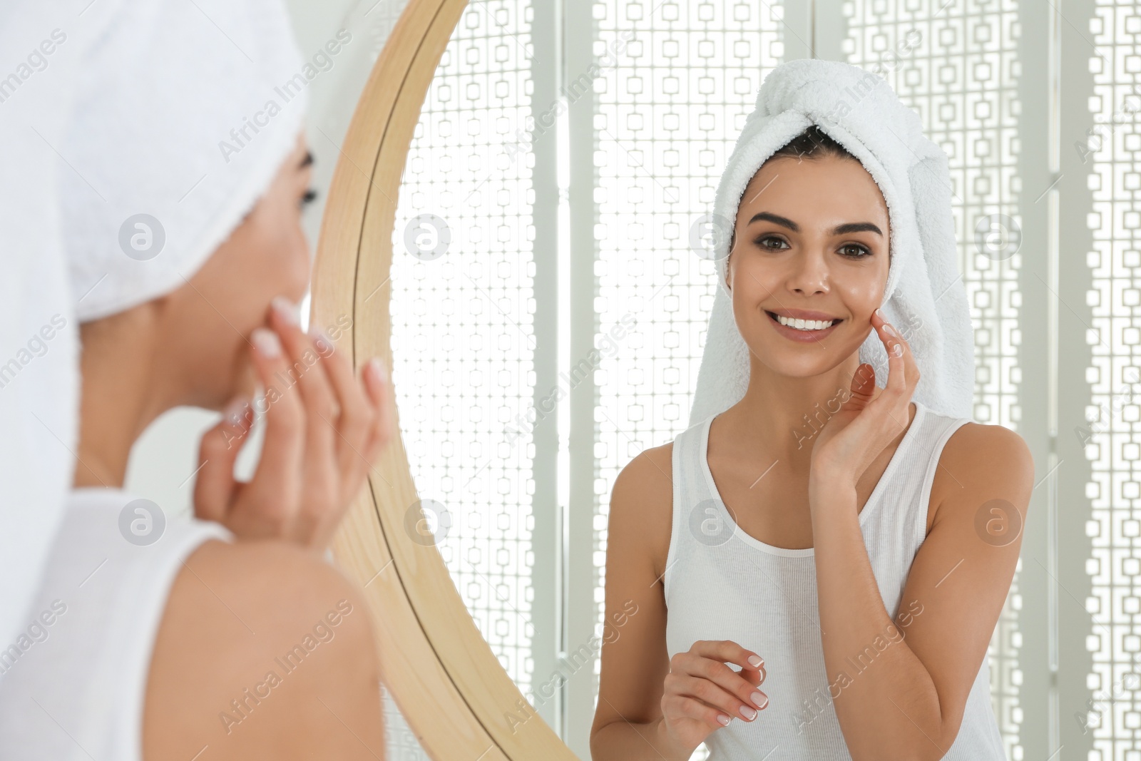 Photo of Happy young woman with clean skin looking at mirror in bathroom