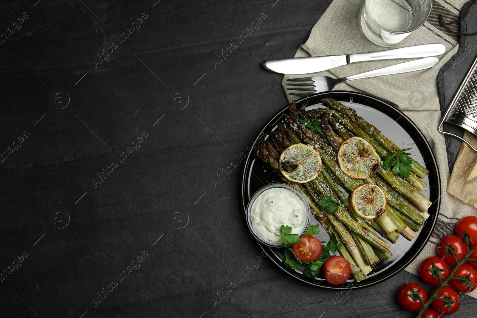 Photo of Oven baked asparagus with lemon slices served on black table, flat lay. Space for text