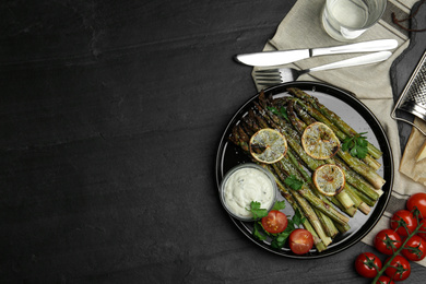 Oven baked asparagus with lemon slices served on black table, flat lay. Space for text