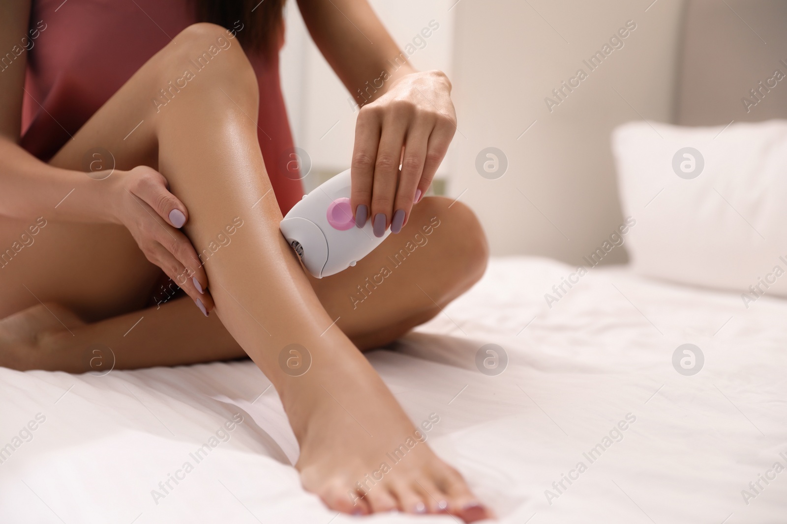 Image of Young woman epilating her legs in bedroom, closeup