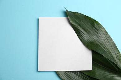 Blank card with tropical leaves on color background, top view