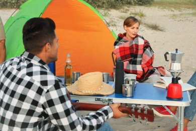 Friends resting near camping tent on sandy beach