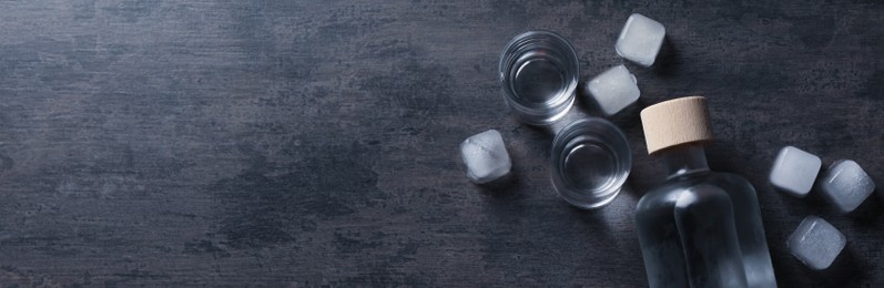 Image of Bottle of vodka and shot glasses with ice on dark table, flat lay with space for text. Banner design