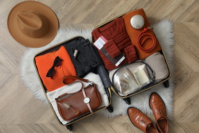 Photo of Open suitcase with folded clothes, accessories and shoes on floor, flat lay