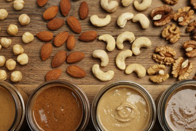 Nut butters in bowls and ingredients on wooden table, flat lay