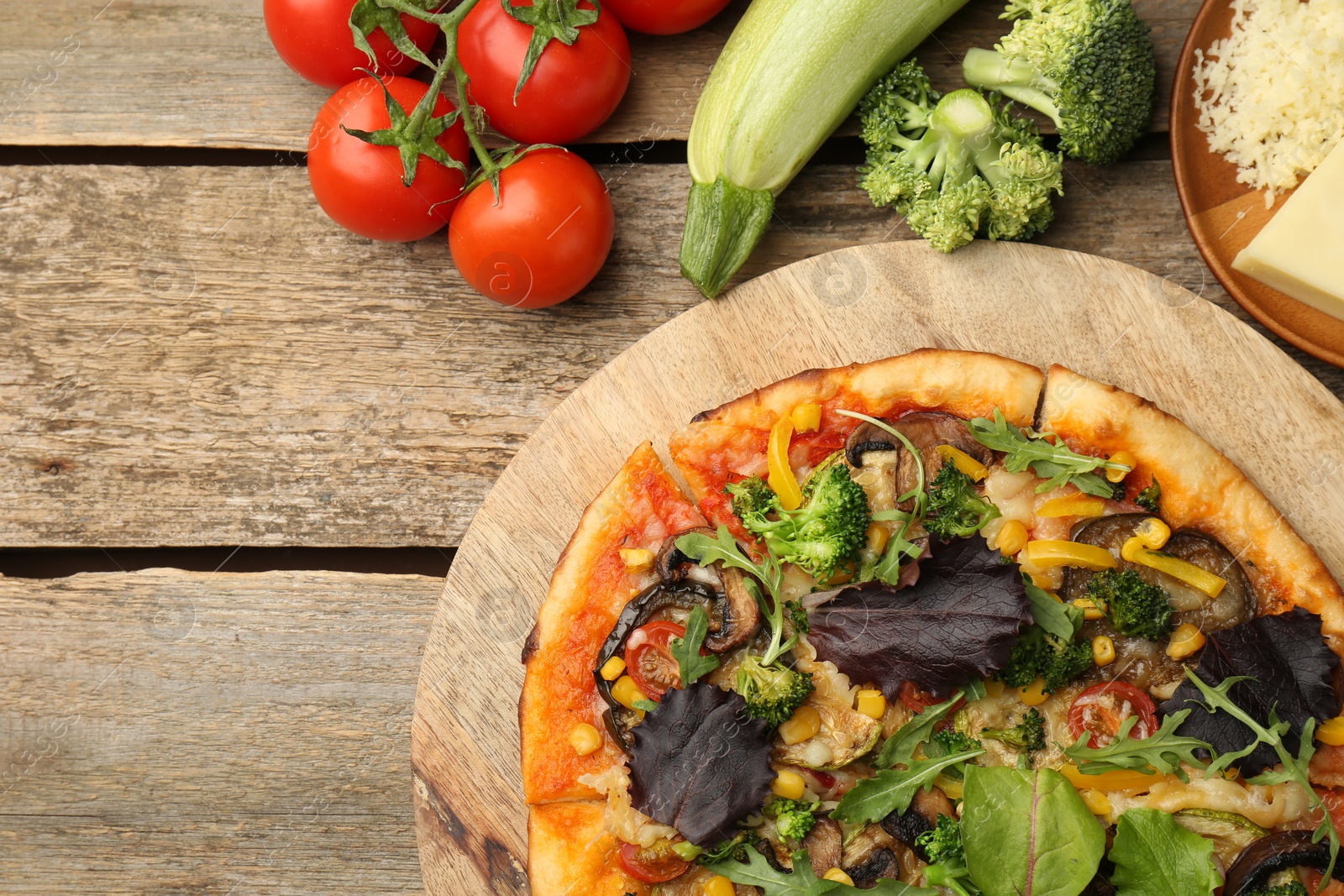 Photo of Delicious vegetarian pizza and ingredients on wooden table, top view. Space for text