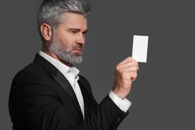 Handsome businessman holding blank business card on grey background