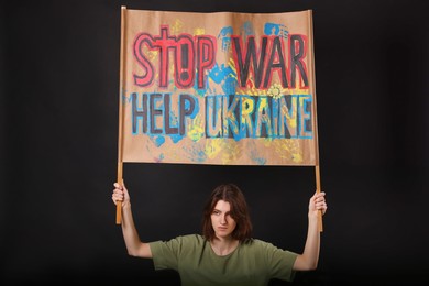Sad woman holding placard with words Stop War Help Ukraine on black background