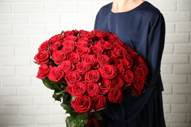 Photo of Woman holding luxury bouquet of fresh red roses near white brick wall, closeup