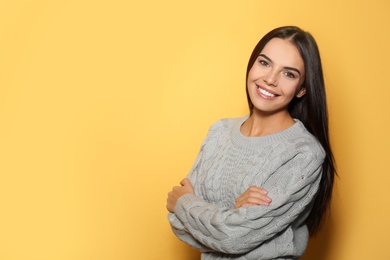 Happy young woman wearing warm sweater on yellow background. Space for text