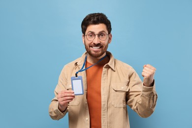 Happy man showing VIP pass badge on light blue background