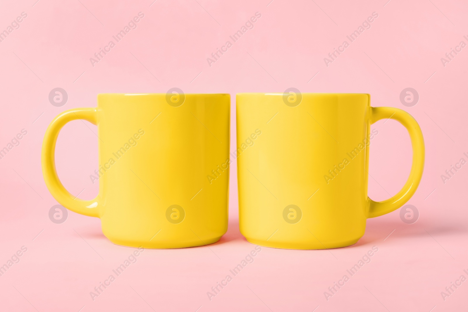 Photo of Two yellow ceramic mugs on pink background