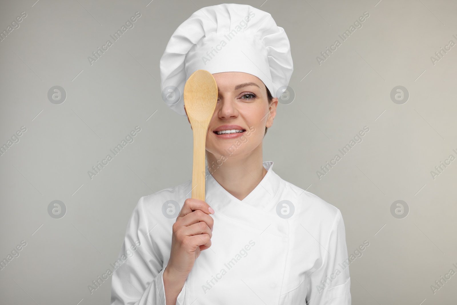 Photo of Happy woman chef in uniform holding wooden spoon on grey background