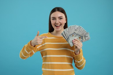 Happy woman pointing at dollar banknotes on light blue background