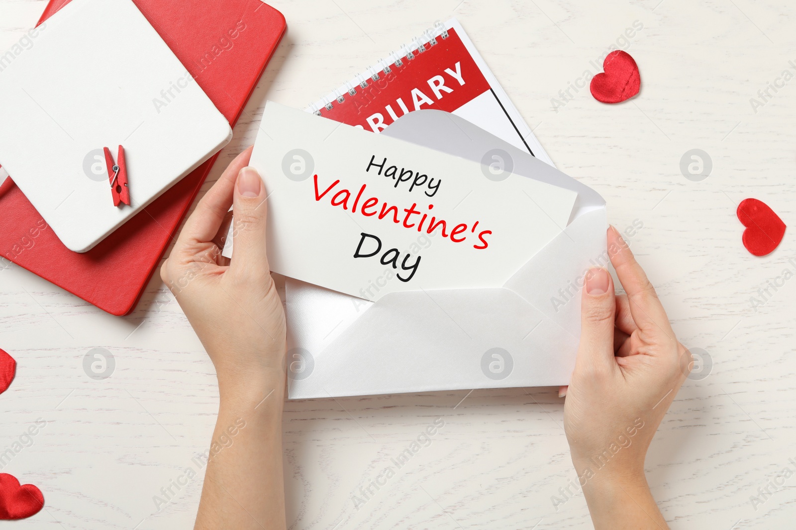 Image of Happy Valentine's Day. Woman putting greeting card into envelope at white wooden table, top view