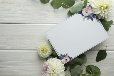 Photo of Blank invitation card and beautiful flowers on white wooden background, flat lay. Space for text