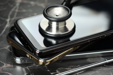 Photo of Stack of modern smartphones and stethoscope on black table, closeup