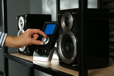 Photo of Woman using remote to control audio speakers indoors, closeup