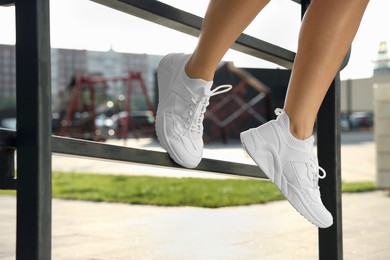 Photo of Woman in stylish sneakers sitting on railing outdoors, closeup