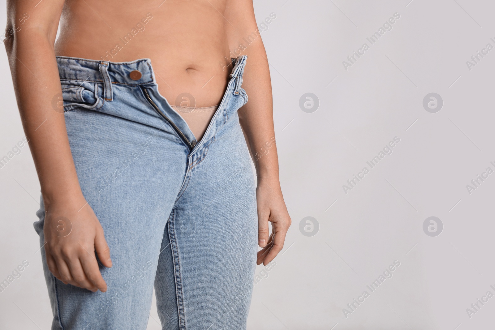 Photo of Woman in unfit jeans on light background, closeup. Space for text