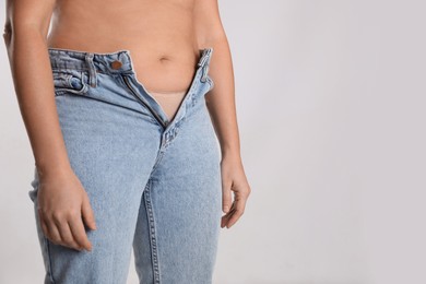 Photo of Woman in unfit jeans on light background, closeup. Space for text