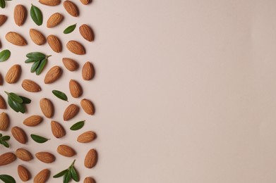 Delicious almonds and fresh leaves on beige background, flat lay. Space for text