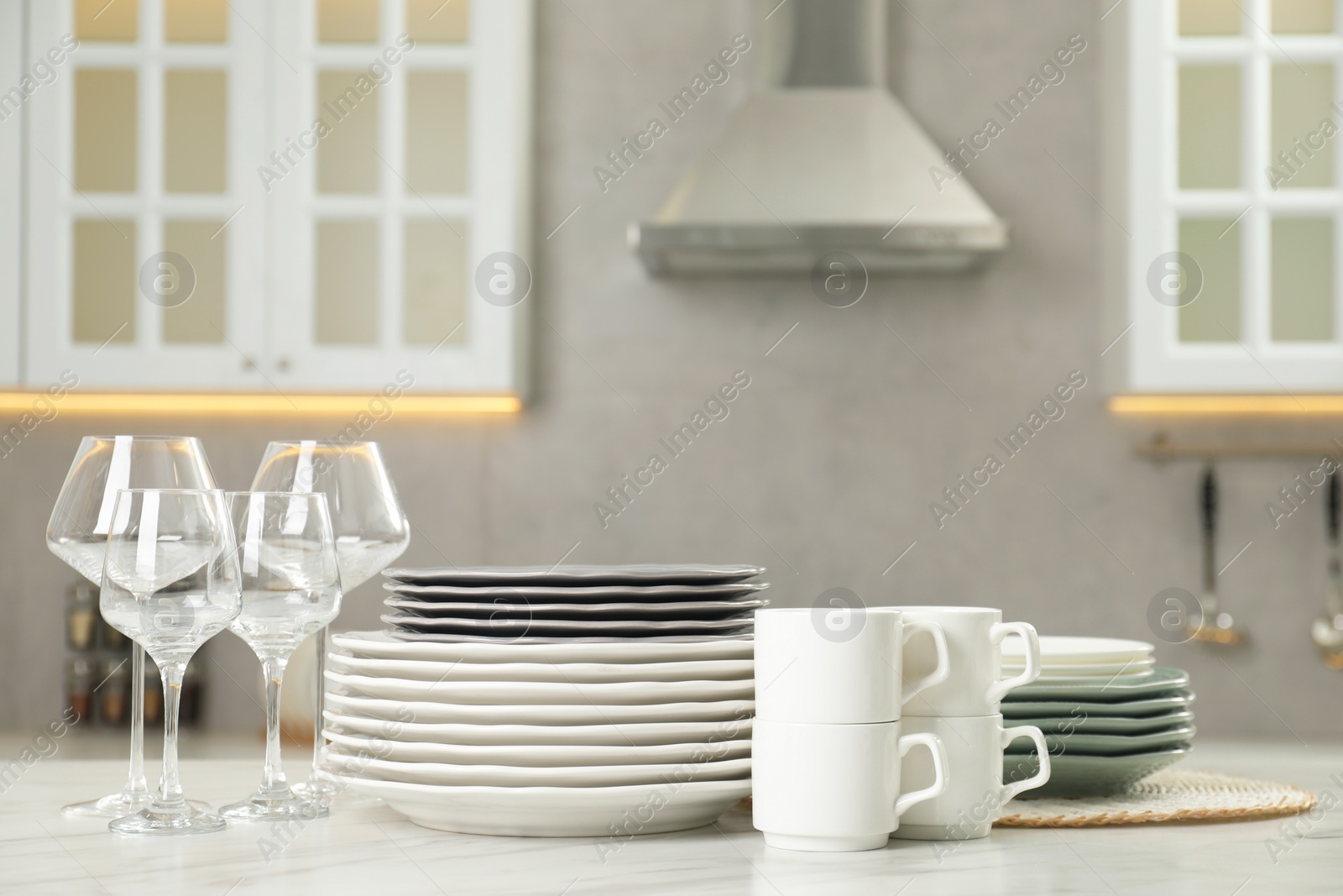 Photo of Clean plates, cups and glasses on white marble table in kitchen