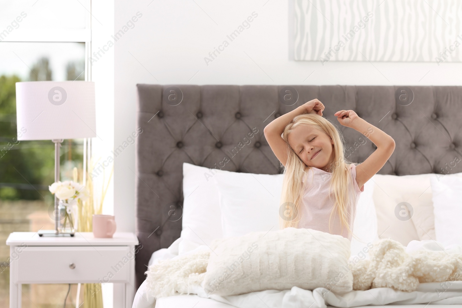 Photo of Cute little girl stretching in bed with pillows at home
