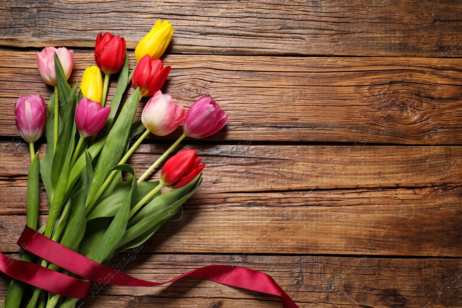 Photo of Beautiful colorful tulip flowers and ribbon on wooden table, flat lay. Space for text