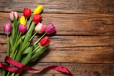 Photo of Beautiful colorful tulip flowers and ribbon on wooden table, flat lay. Space for text