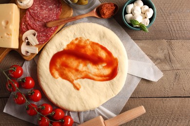 Photo of Pizza dough with tomato sauce and products on wooden table, flat lay