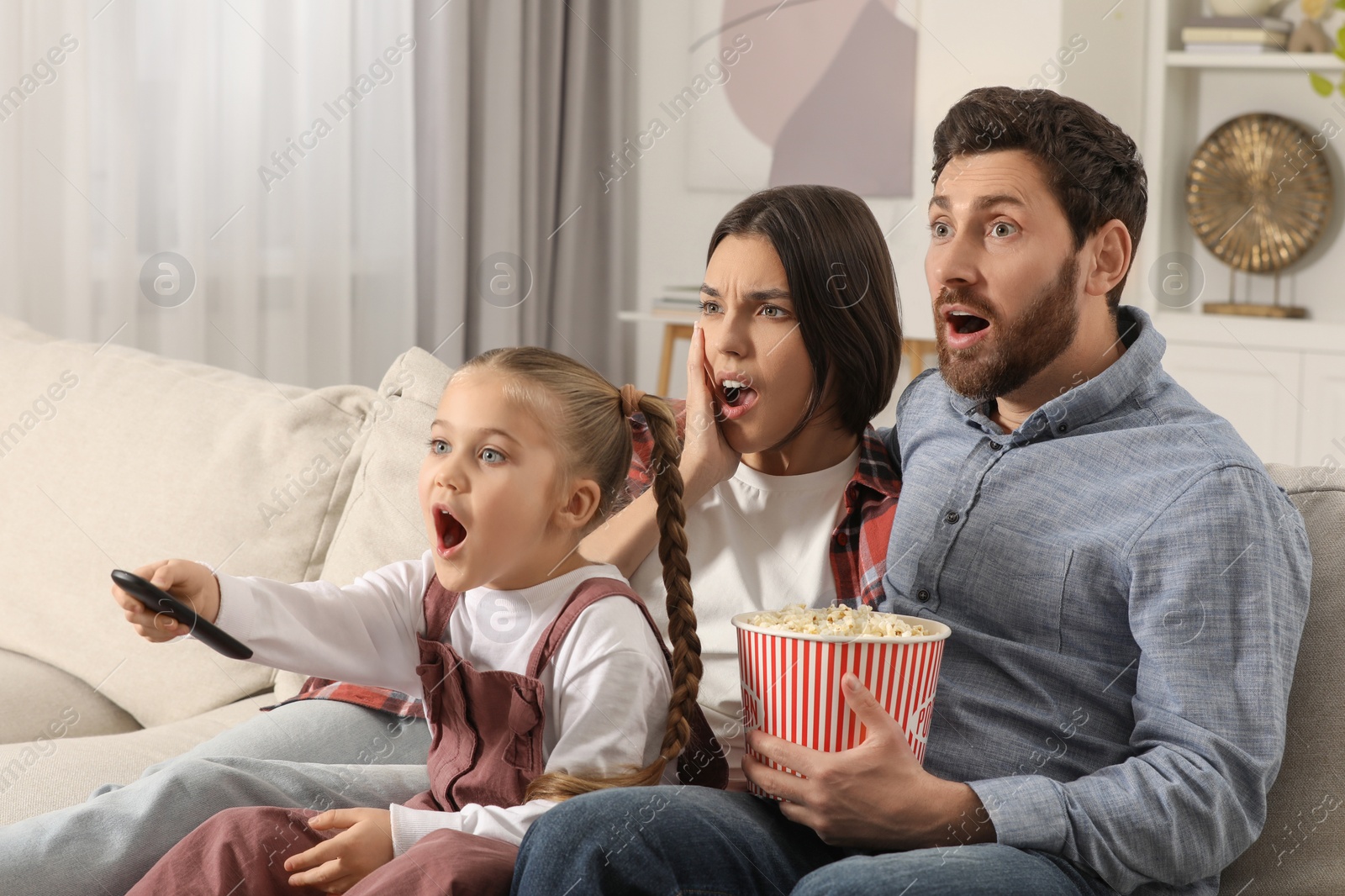 Photo of Surprised family watching TV with popcorn on sofa at home