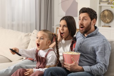 Photo of Surprised family watching TV with popcorn on sofa at home