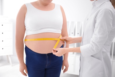 Photo of Doctor measuring waist of overweight woman in clinic, closeup