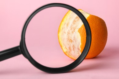 Photo of Cellulite problem. Orange and magnifying glass on pink background, closeup