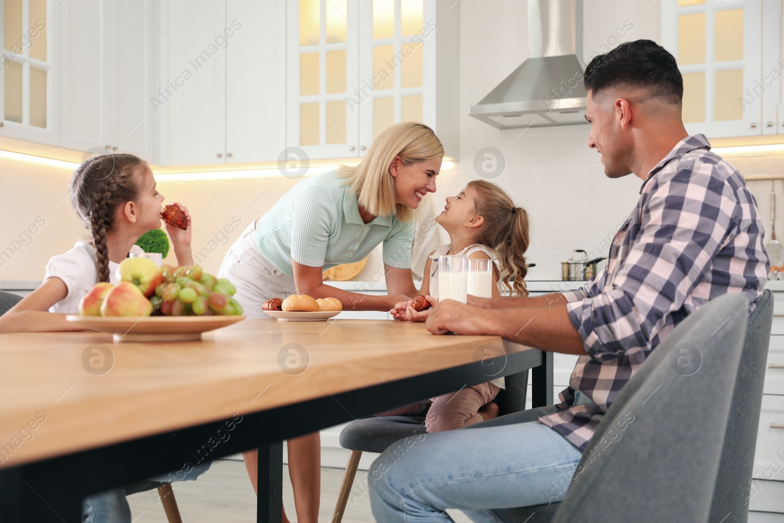 Photo of Happy family eating together at table in modern kitchen