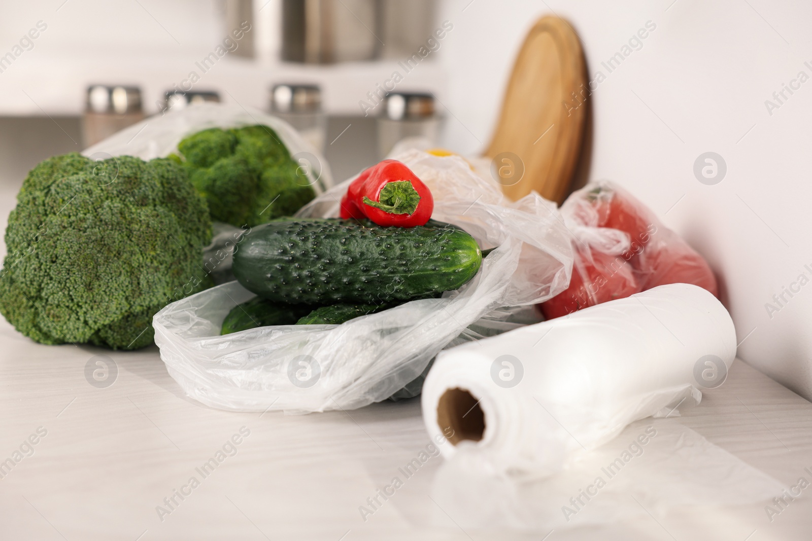 Photo of Roll of plastic bags and fresh vegetables on white table