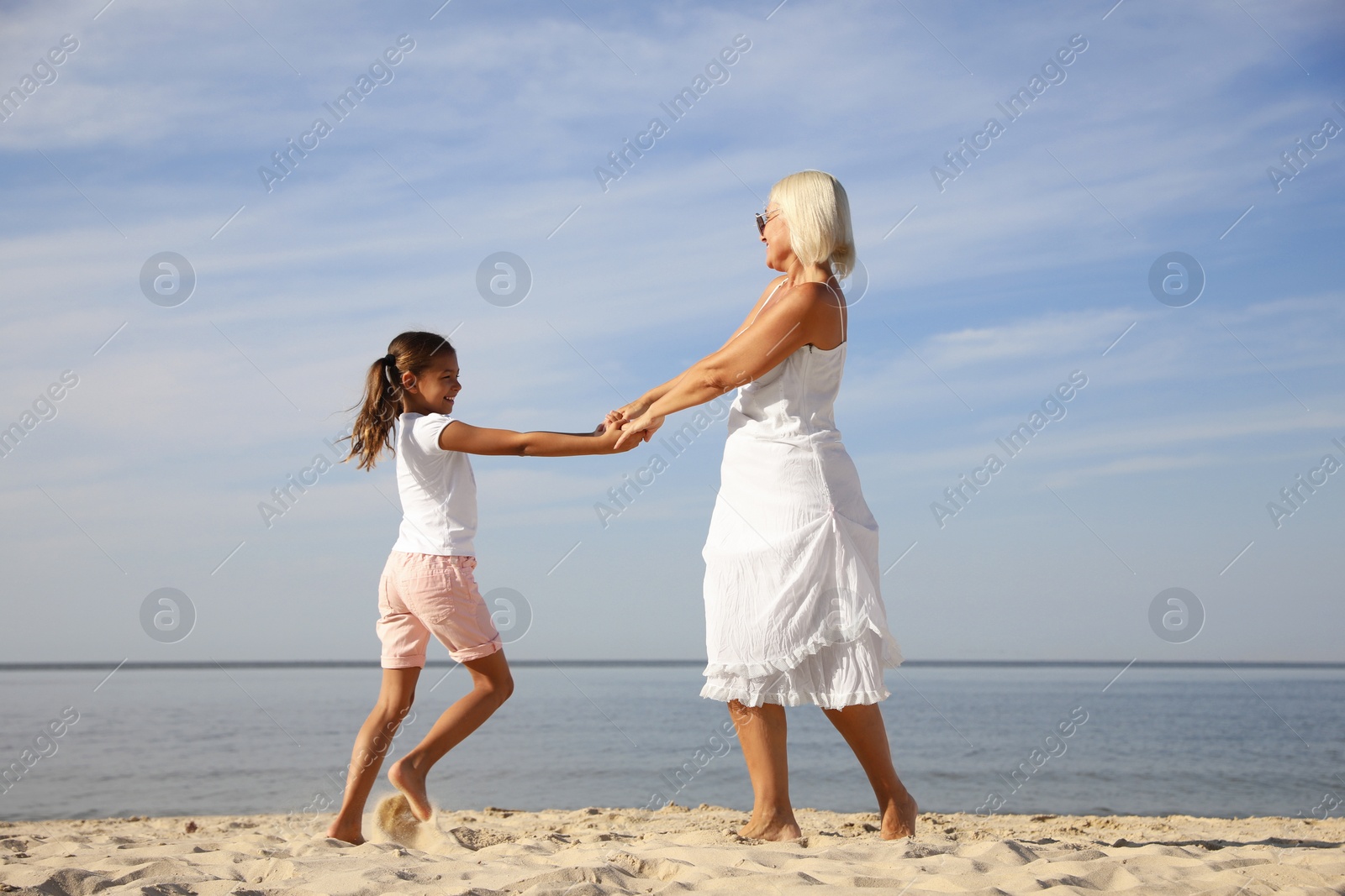 Photo of Cute little girl with grandmother spending time together on sea beach