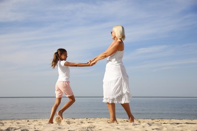 Photo of Cute little girl with grandmother spending time together on sea beach