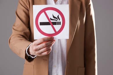 Photo of Woman holding card with no smoking sign on gray background, closeup