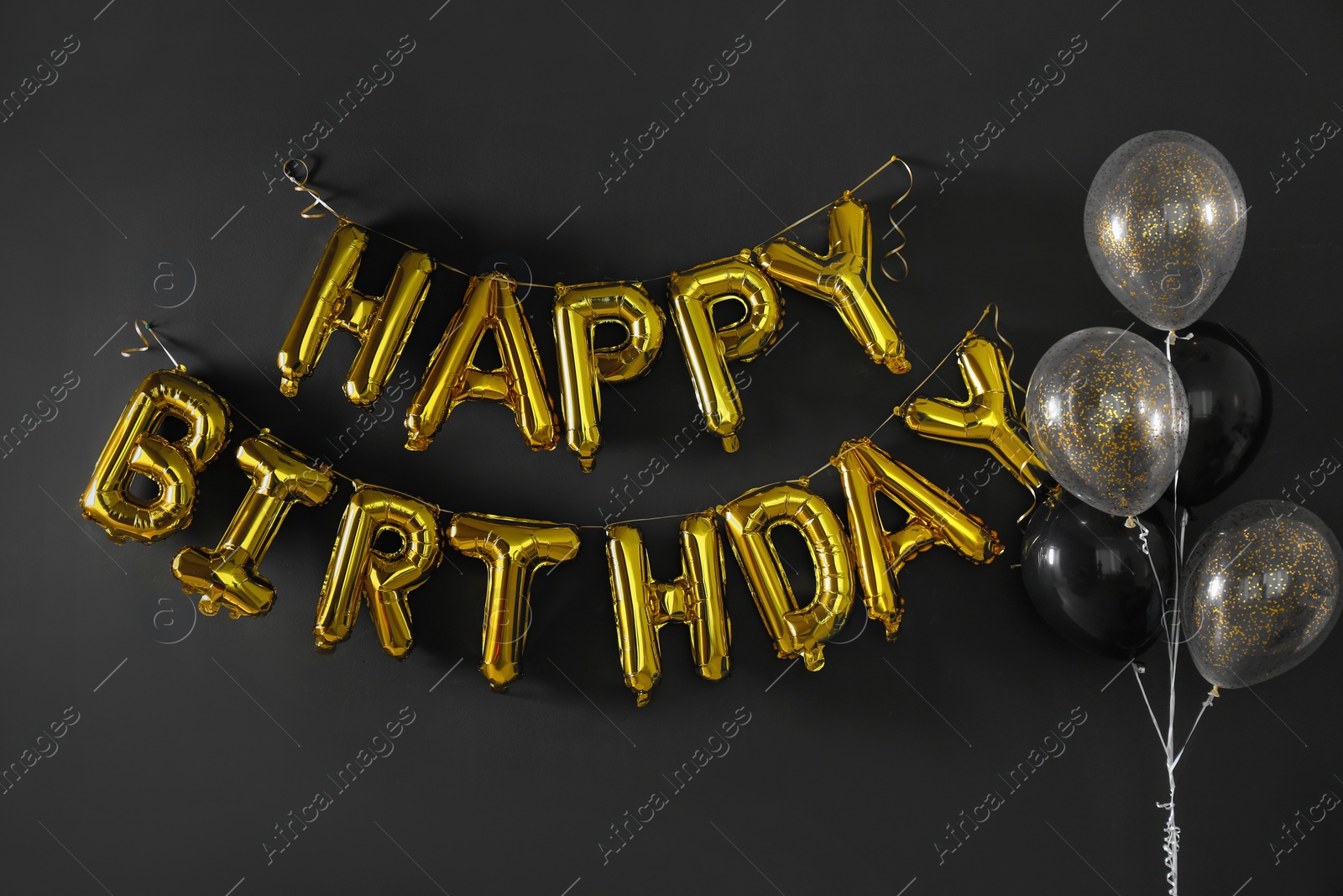 Photo of Phrase HAPPY BIRTHDAY made of golden balloon letters on black wall