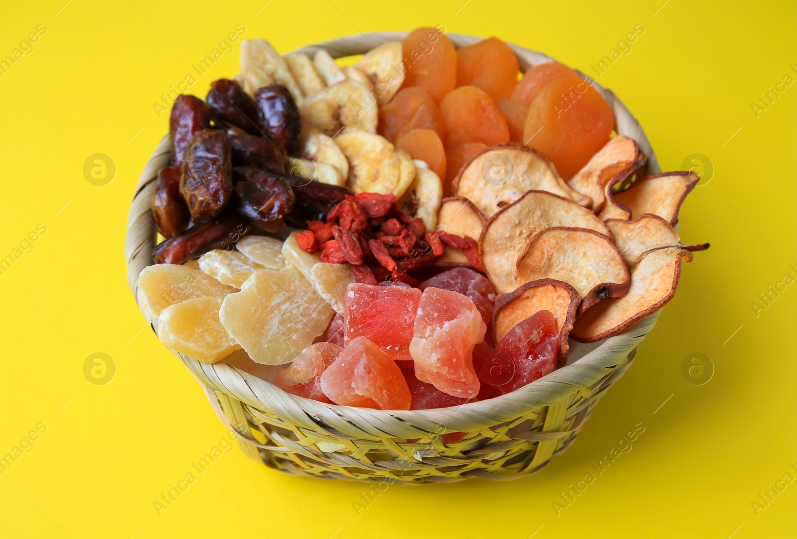 Photo of Wicker basket with different dried fruits on yellow background