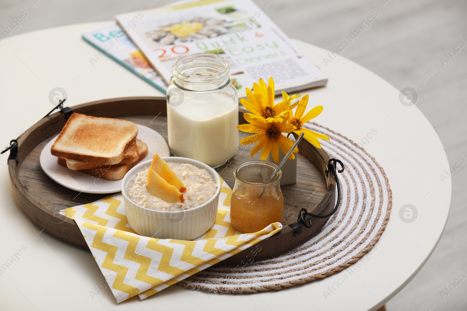 Photo of Wooden tray with delicious breakfast and beautiful flowers on white table indoors