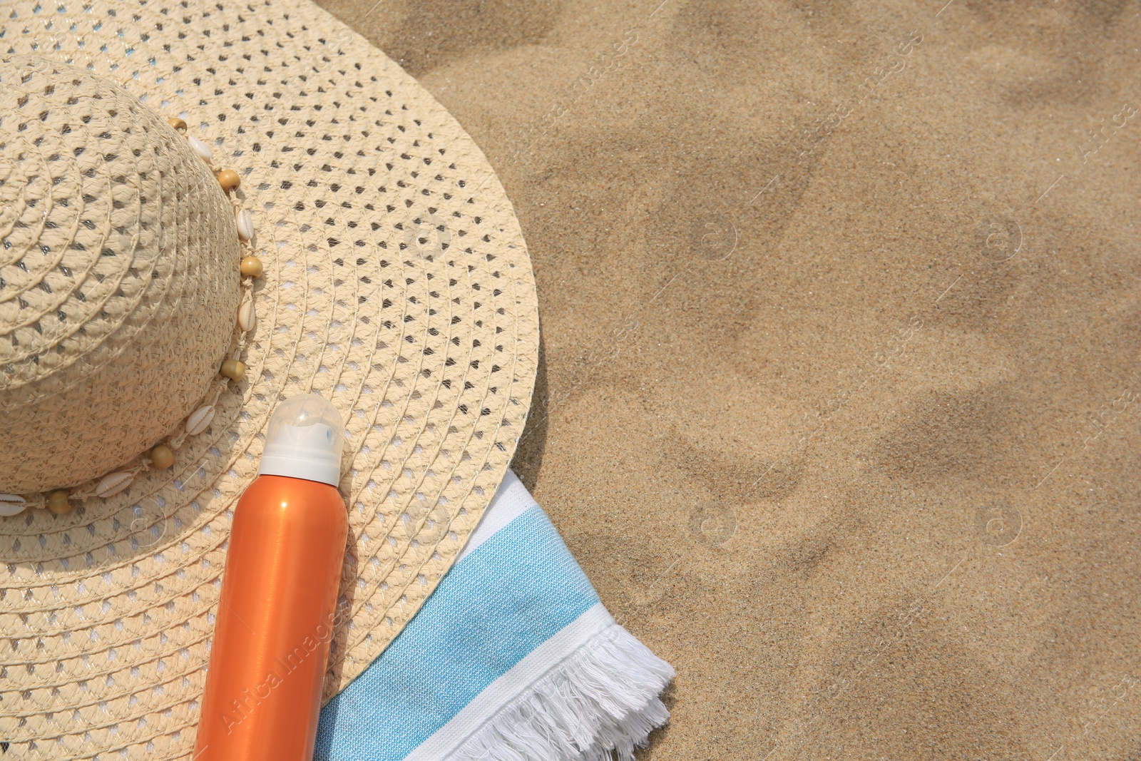 Photo of Sunscreen, hat and towel on sand, above view with space for text. Sun protection care