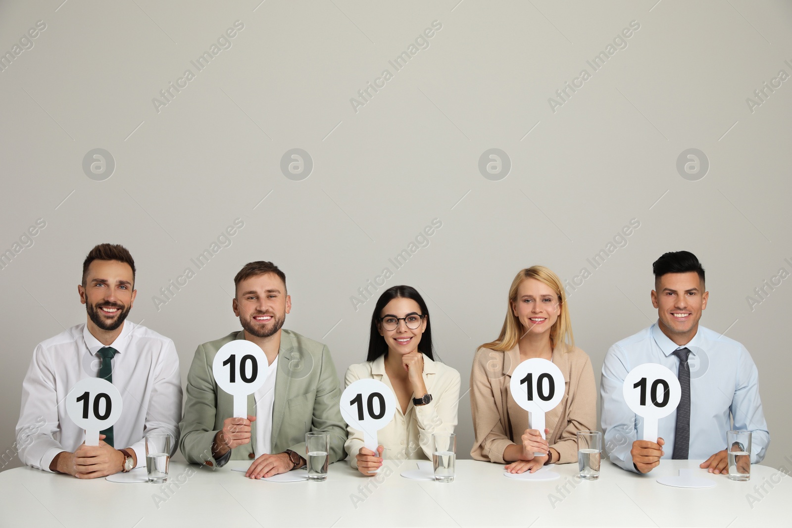 Photo of Panel of judges holding signs with highest score at table on beige background