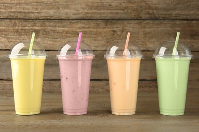 Plastic cups with different tasty smoothies on wooden table