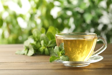 Photo of Glass cup of aromatic green tea with fresh mint on wooden table against blurred background. Space for text