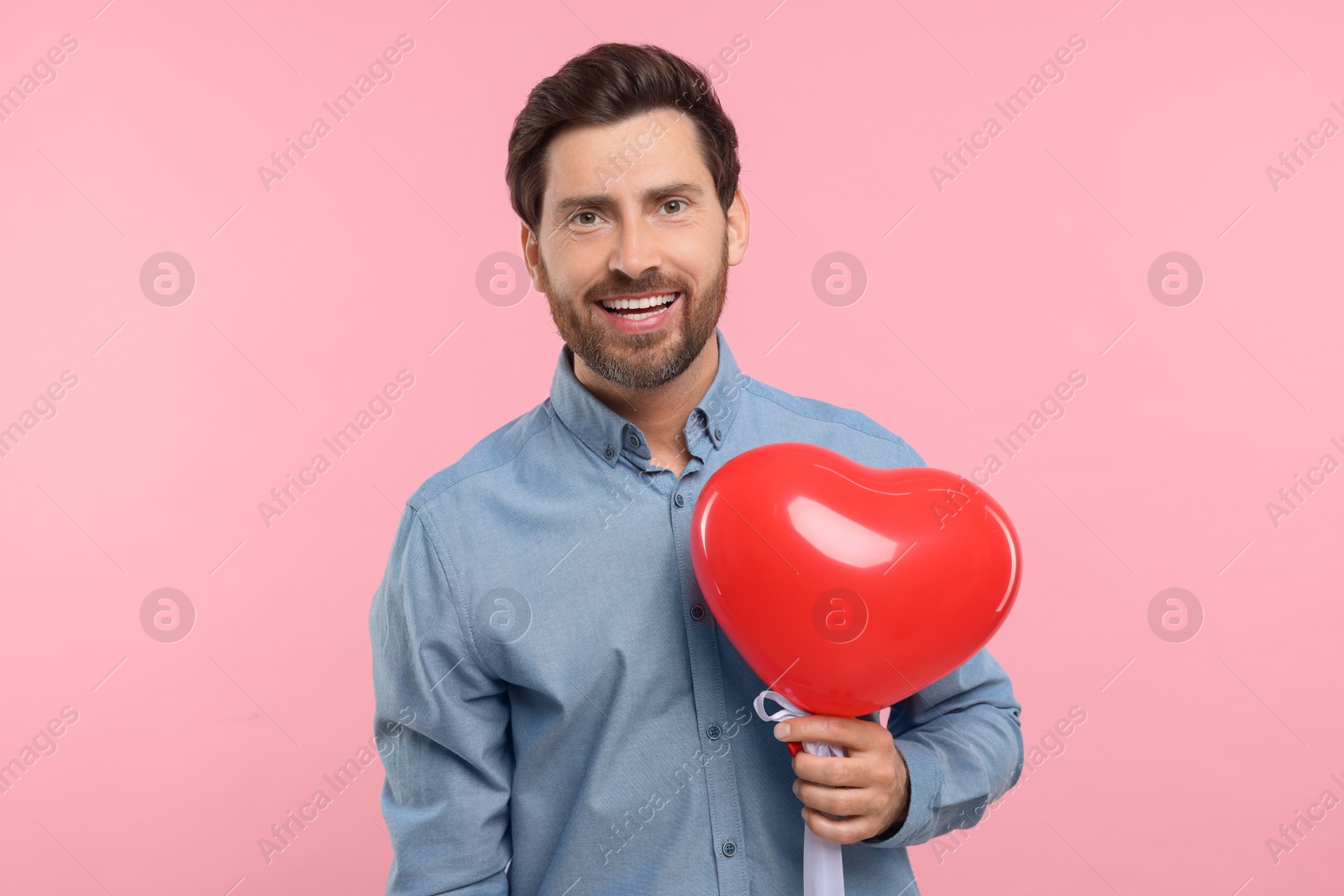 Photo of Happy man holding red heart shaped balloon on pink background