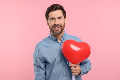 Photo of Happy man holding red heart shaped balloon on pink background