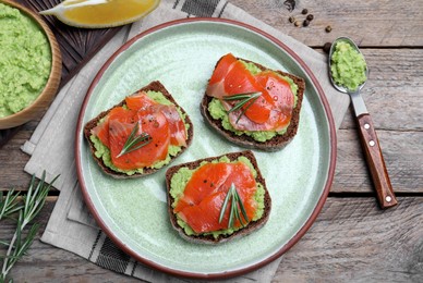 Photo of Delicious sandwiches with salmon, avocado and rosemary served on wooden table, flat lay